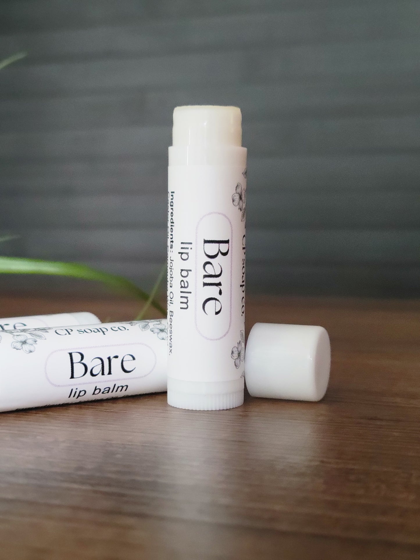 Two lip balm tubes labeled 'Bare' on a wooden surface with a blurred background.