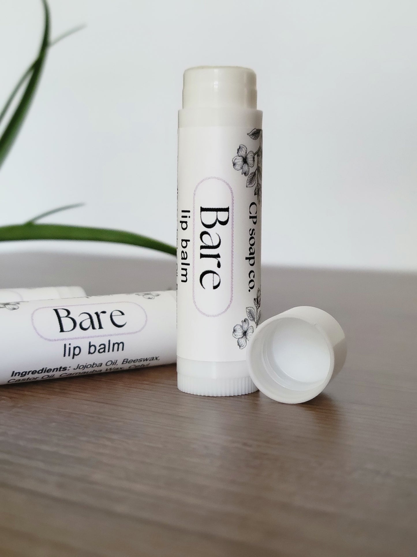 Two lip balms labeled 'Bare' on a light wooden surface with a white background.
