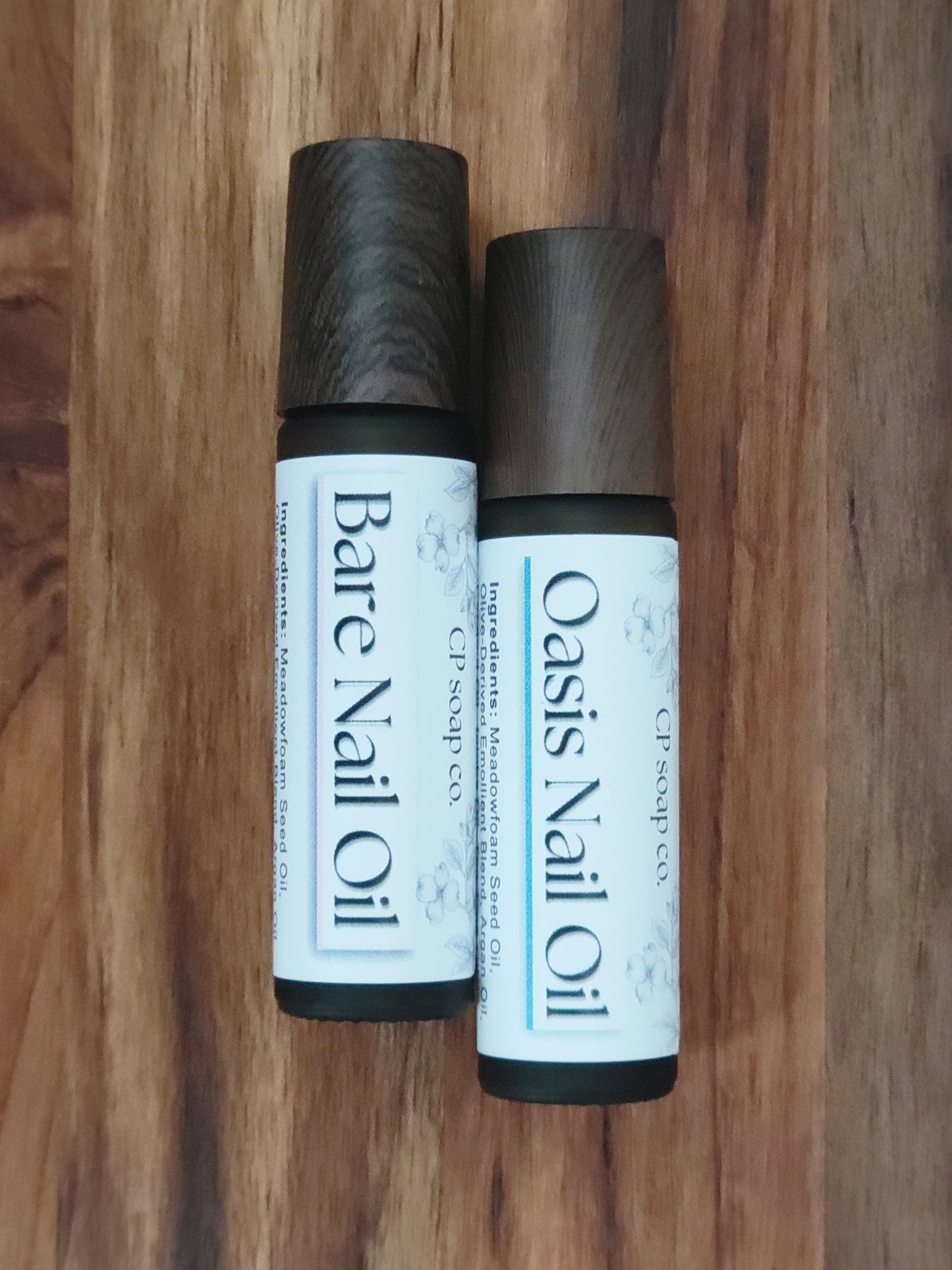 Two bottles of nail oil labeled 'Bare Nail Oil' and 'Oasis Nail Oil' on a wooden surface.