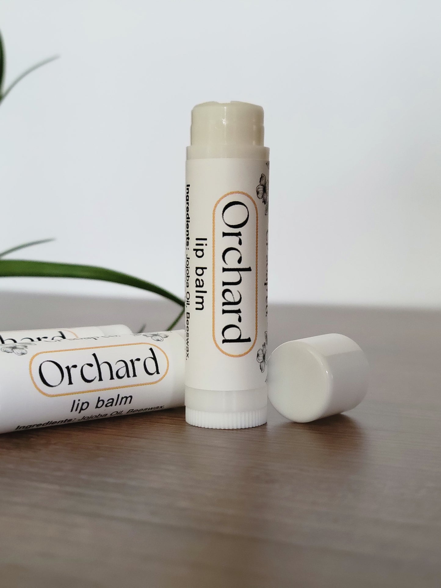 Orchard lip balm on a white surface with a blurred background