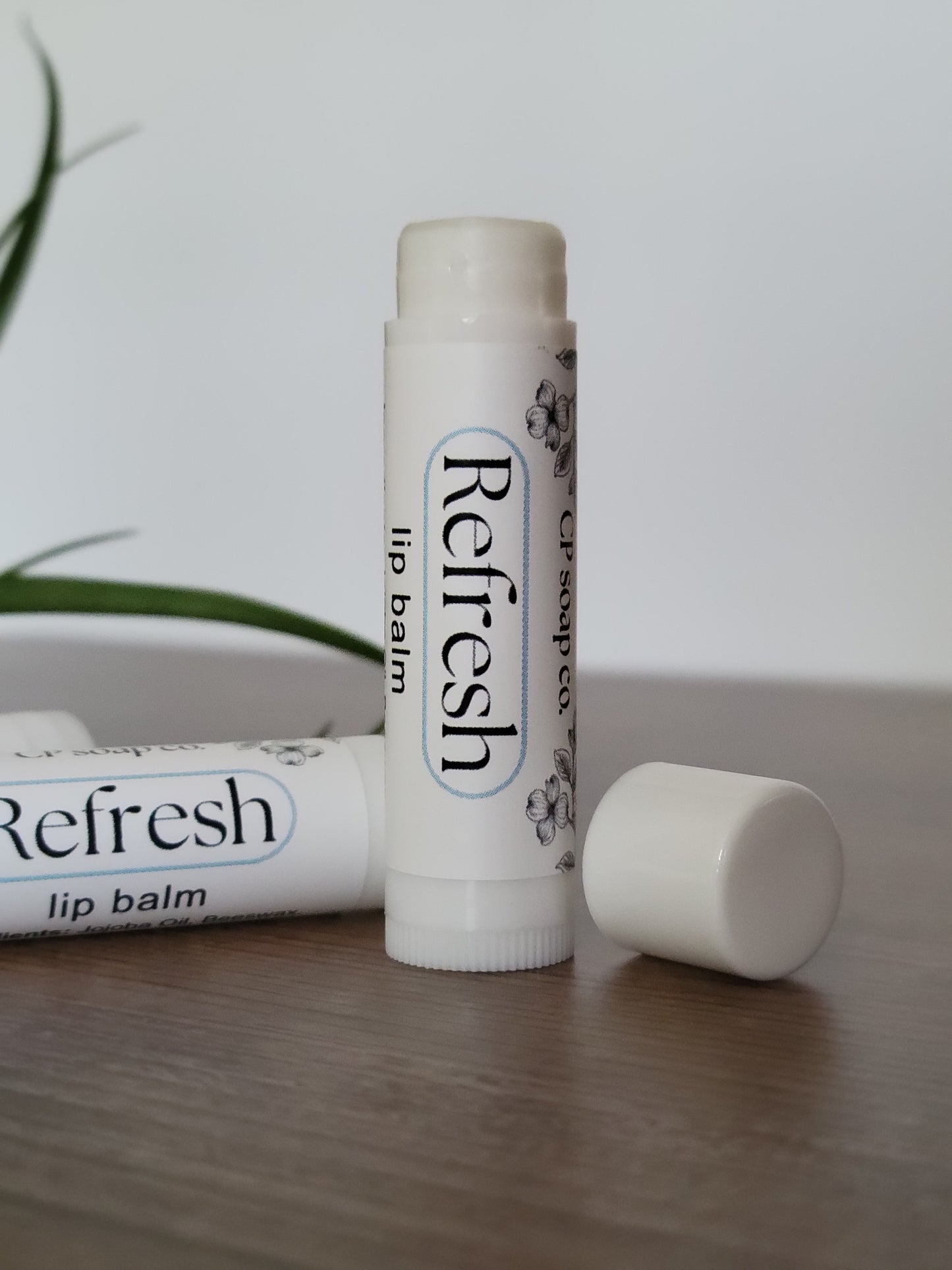 Two lip balms labeled 'Refresh' on a light wooden surface.