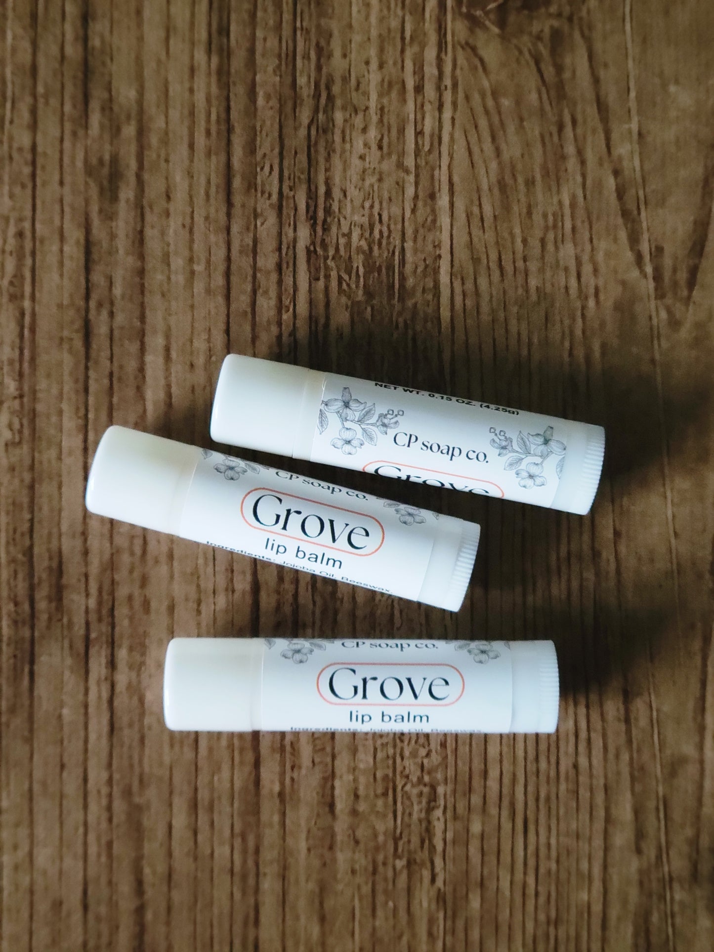 Three Grove lip balms on a wooden surface