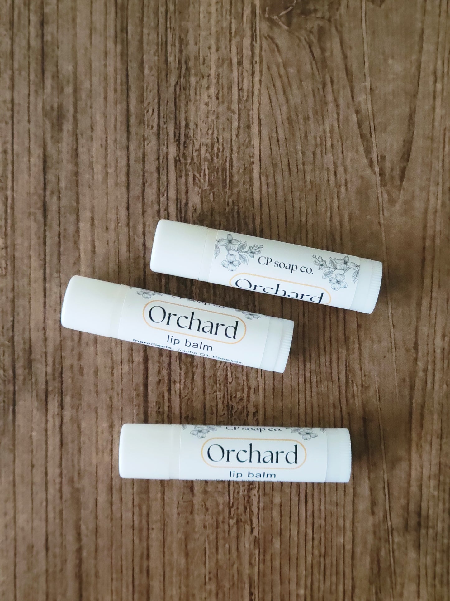 Three Orchard lip balm tubes on a wooden surface