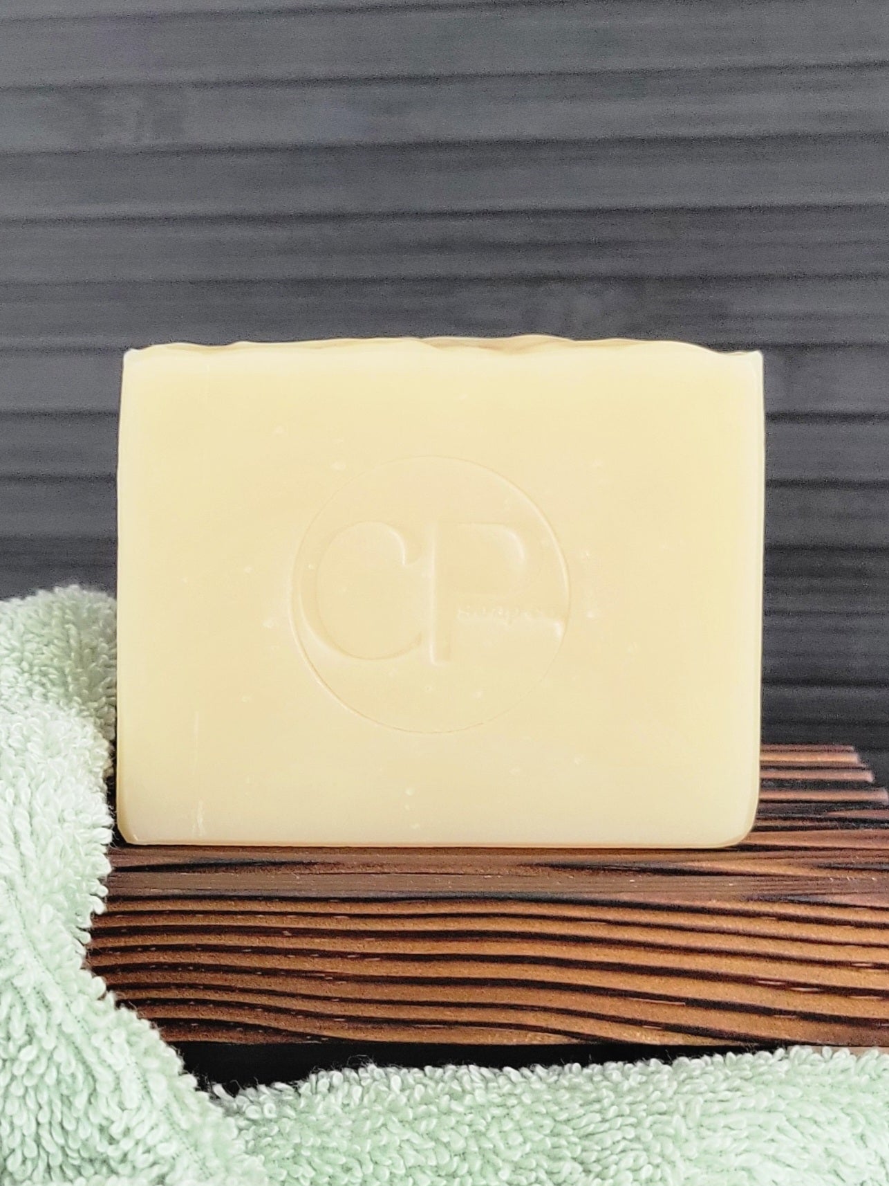 Bar of soap on a wooden soap dish with a green towel underneath