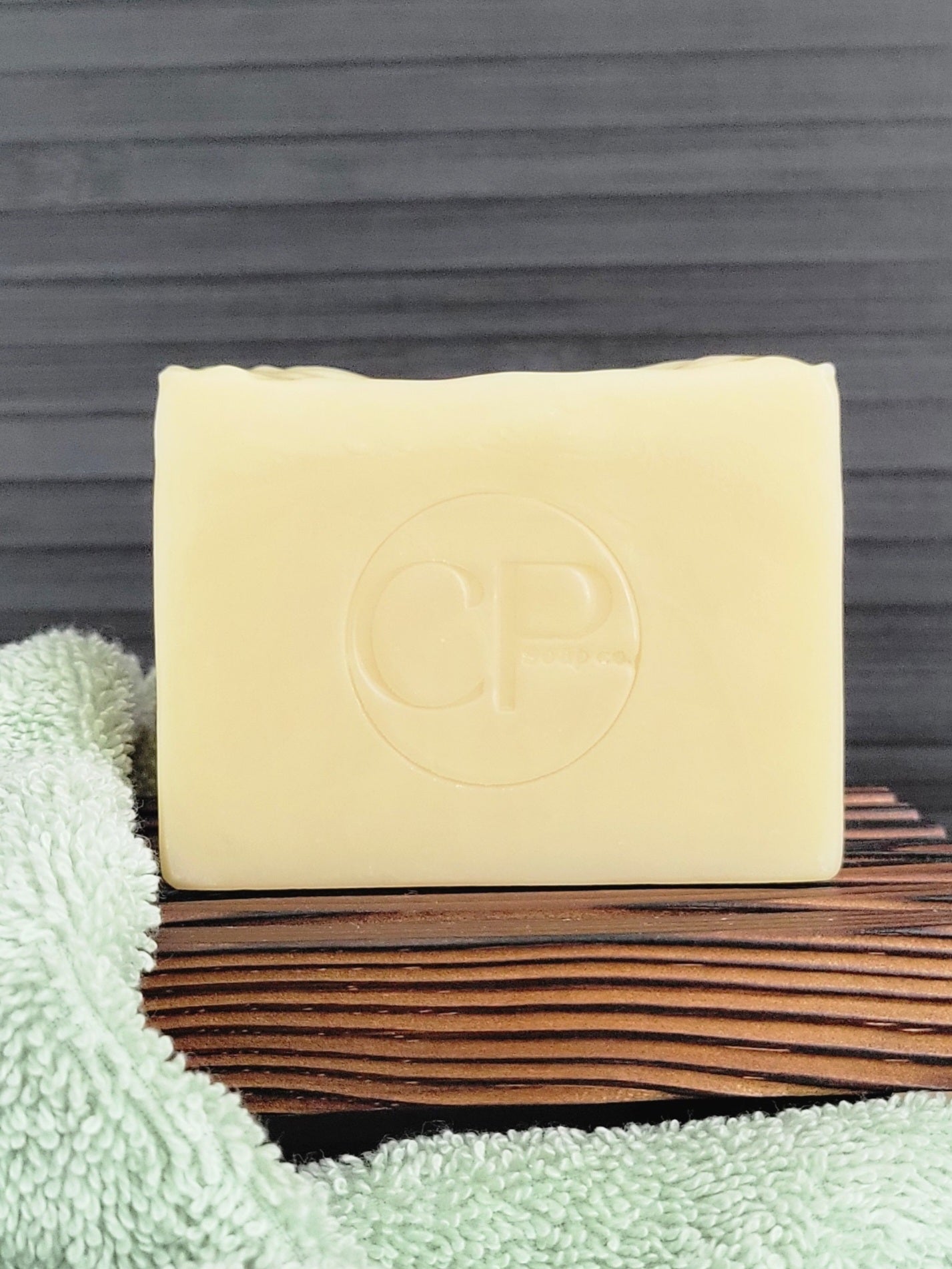 Bar of soap with a brand logo on a wooden surface next to a green towel