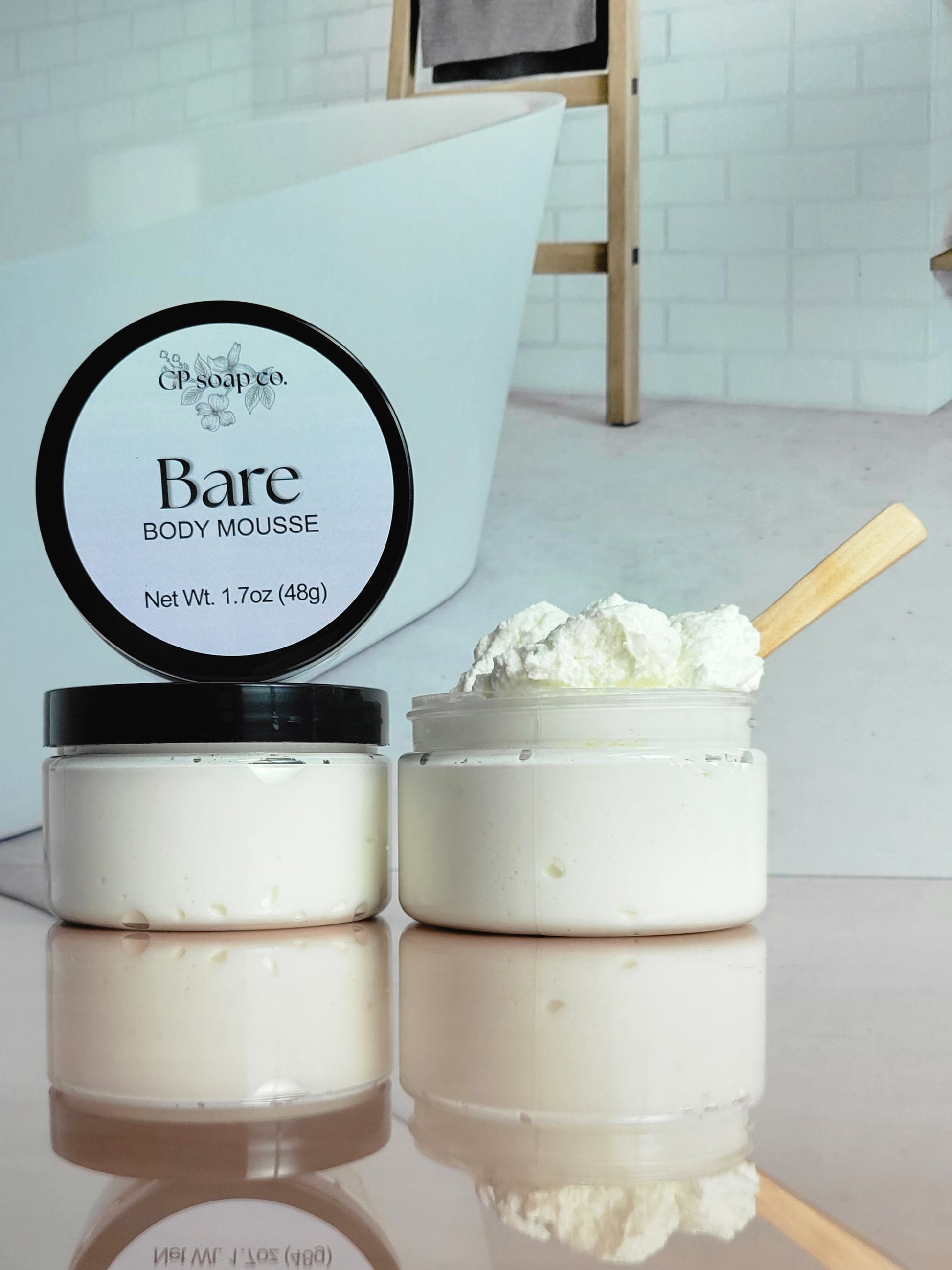 Two jars of Bare Body Mousse with a scoop of mousse on a reflective surface.
