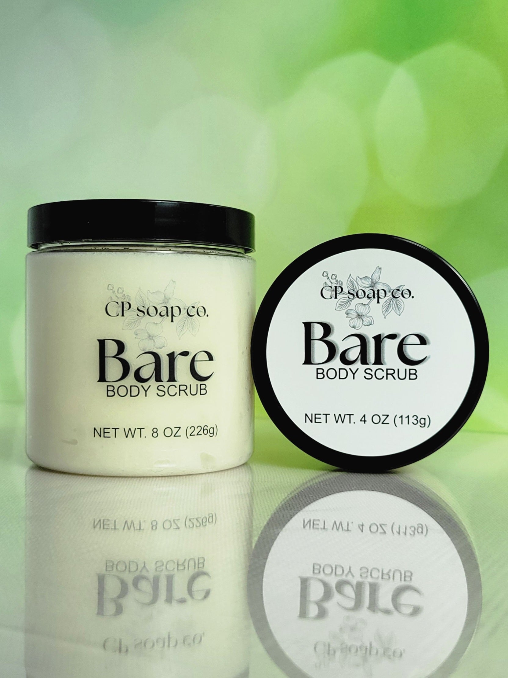 CP Soap Co. Bare Body Scrub jar and round container on a reflective surface with green bokeh background