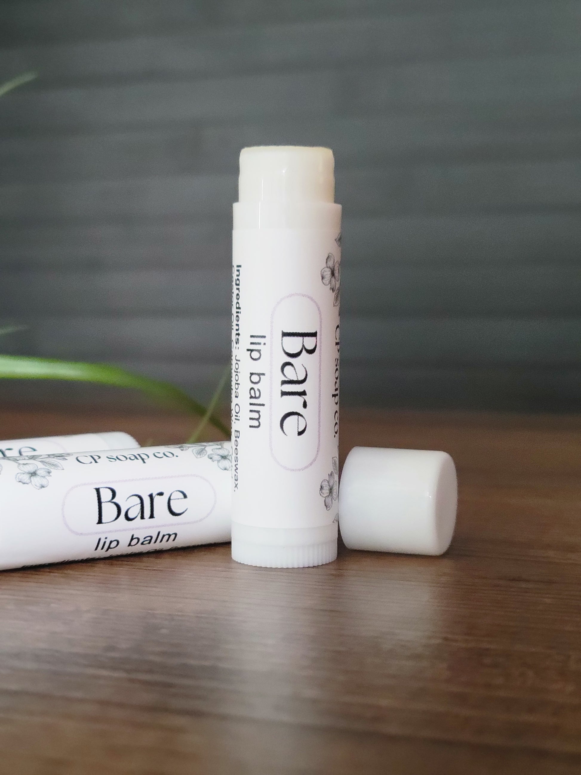Two lip balm tubes labeled 'Bare' on a wooden surface with a blurred background.