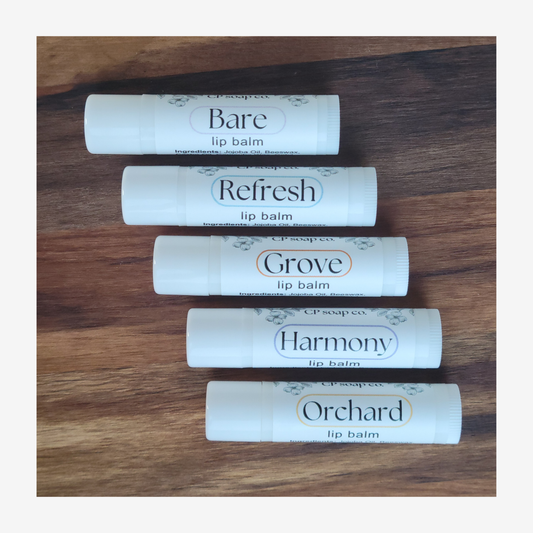 Five lip balm tubes labeled 'Bare', 'Refresh', 'Grove', 'Harmony', and 'Orchard' on a wooden surface.