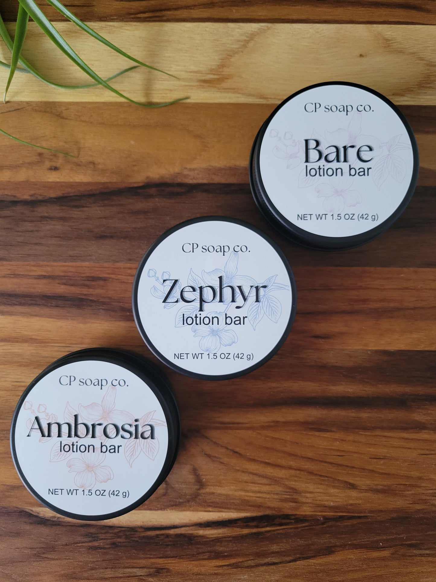 Three CP Soap Co. lotion bars on a wooden surface with grass.