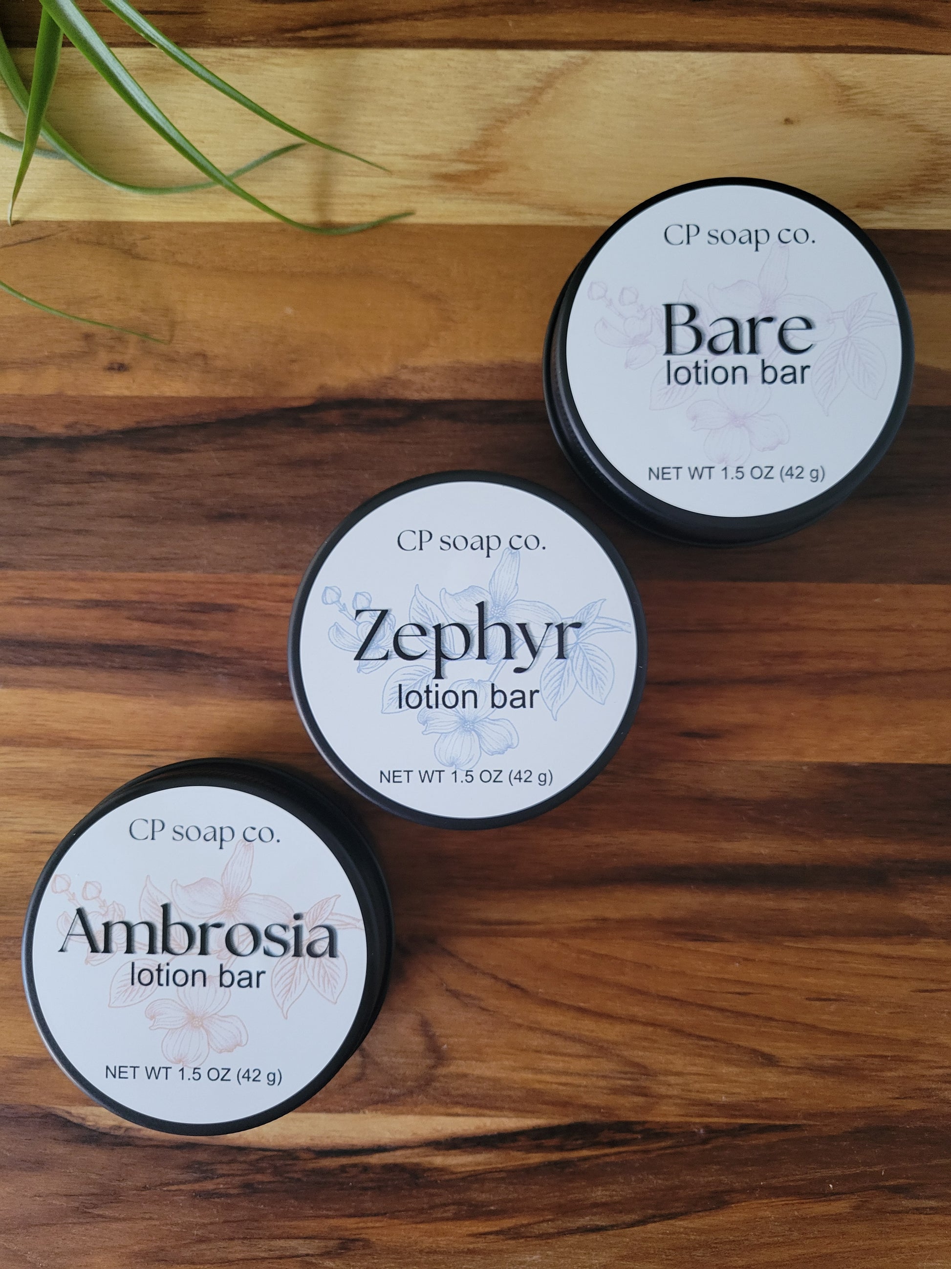 Three CP Soap Co. lotion bars on a wooden surface with grass.