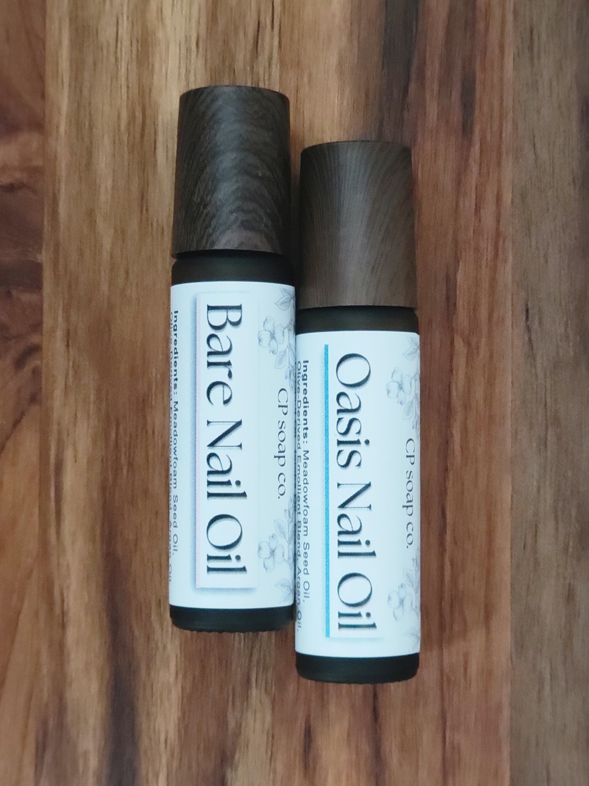 Two bottles of nail oil labeled 'Bare Nail Oil' and 'Oasis Nail Oil' on a wooden surface.