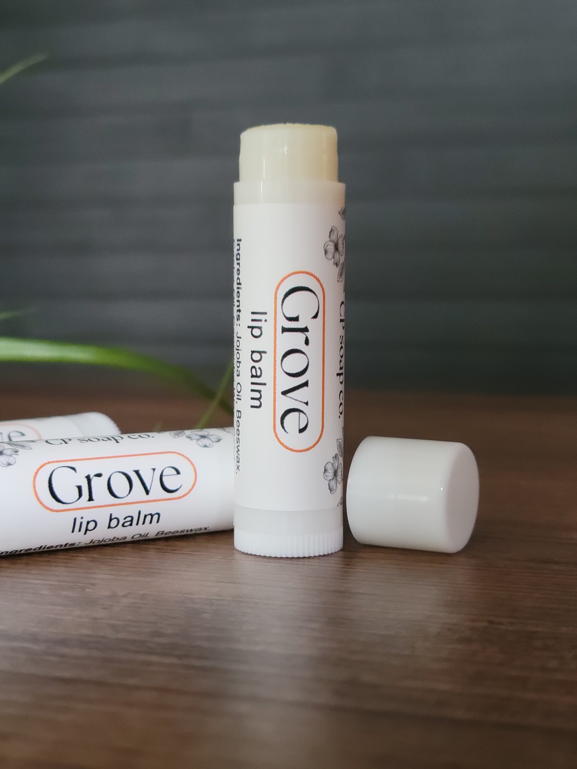 Two Grove lip balm tubes on a wooden surface with a blurred background