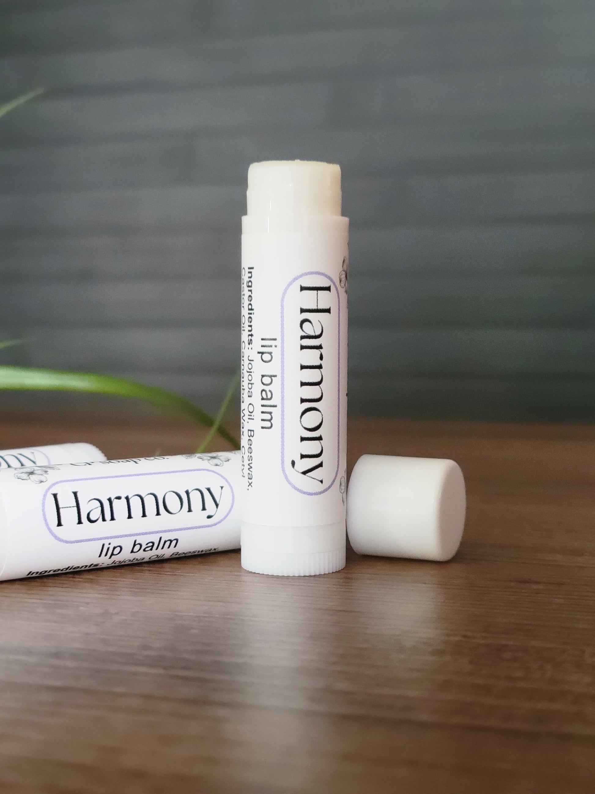 Two lip balms labeled 'Harmony' on a wooden surface with a blurred background.