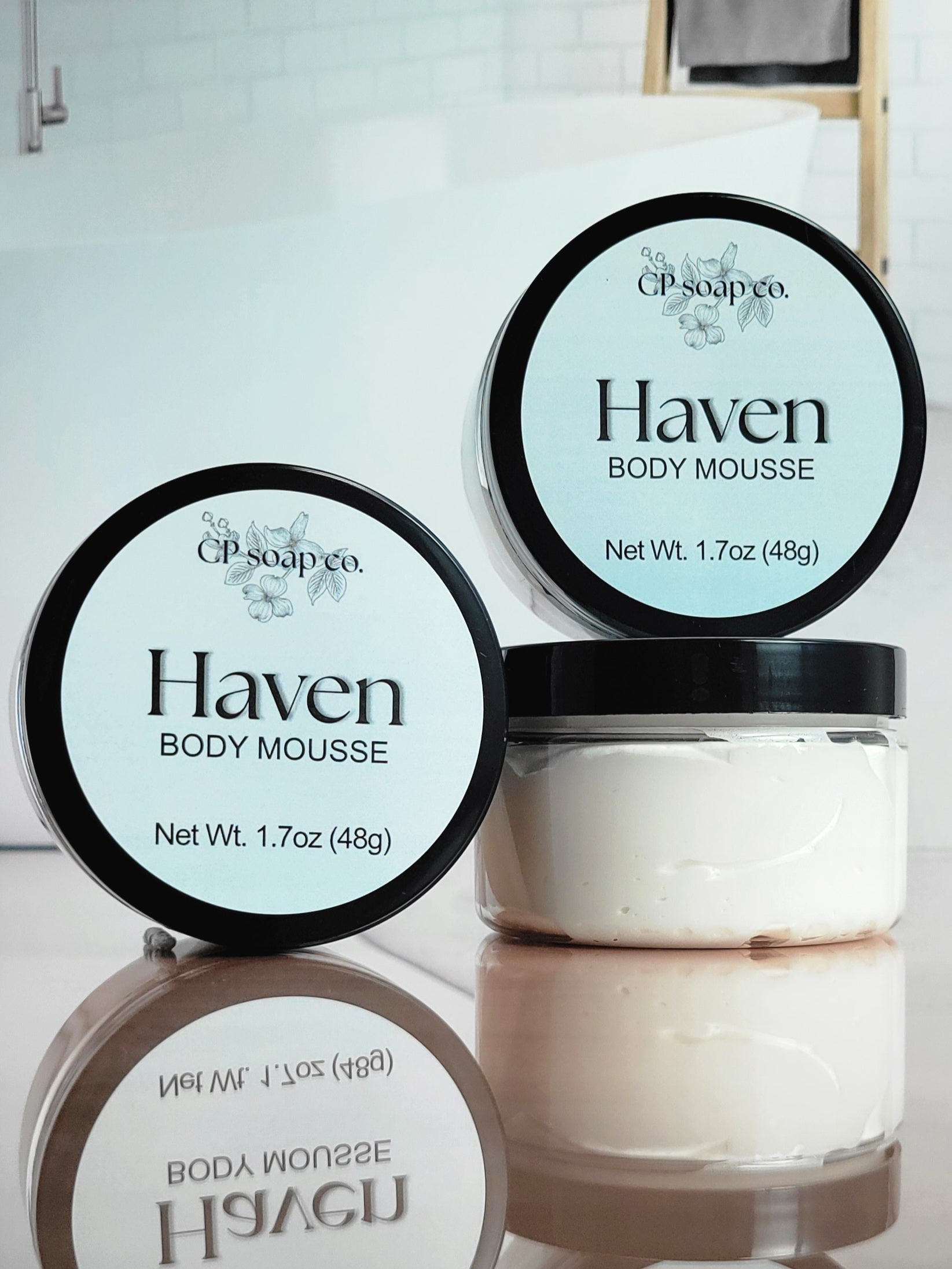 Two jars of Haven Body Mousse by GP Soap Co on a reflective surface with a blurred background.