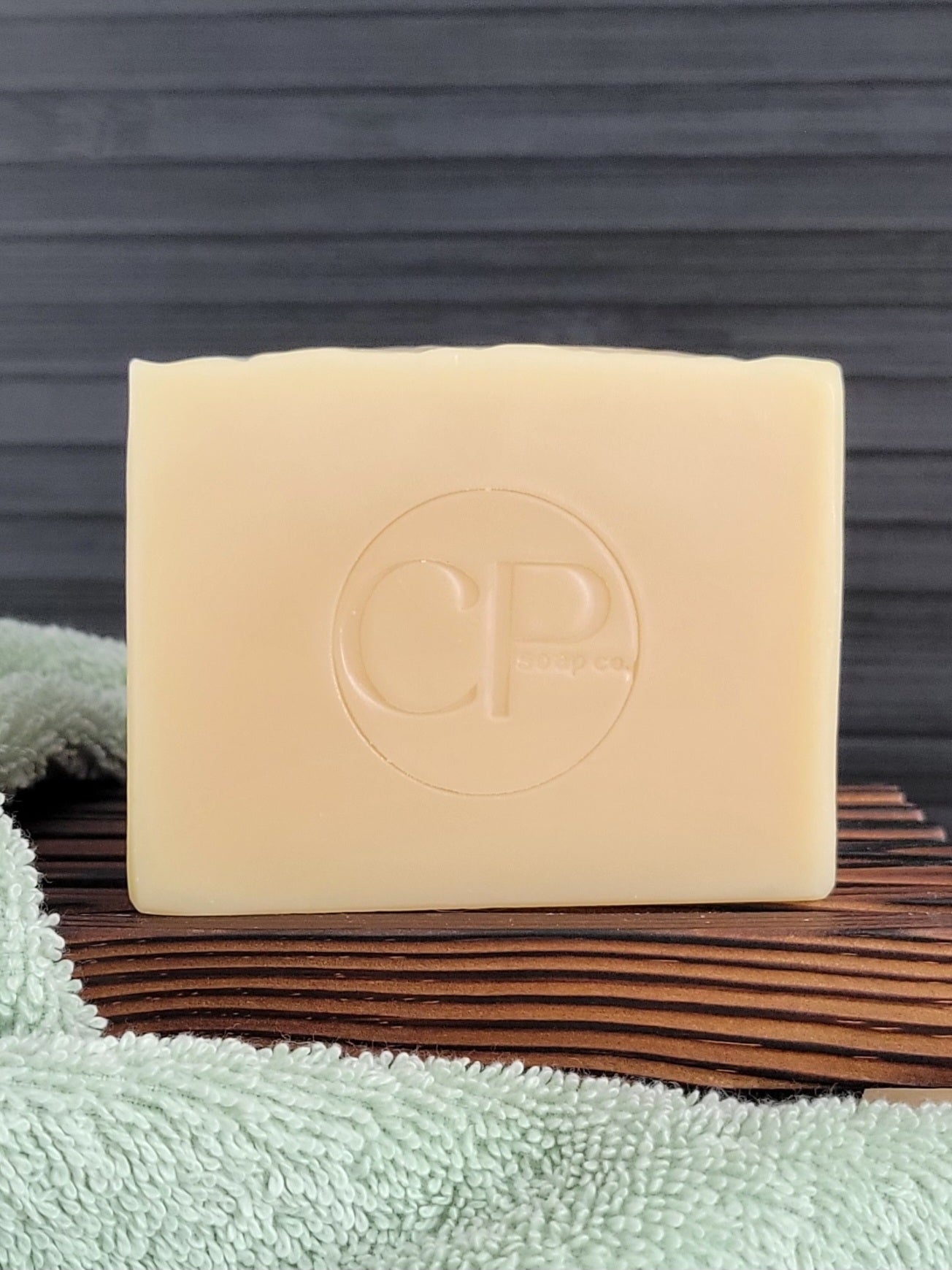 Bar of soap with 'CP' logo on a wooden block, placed on a green towel against a dark background.