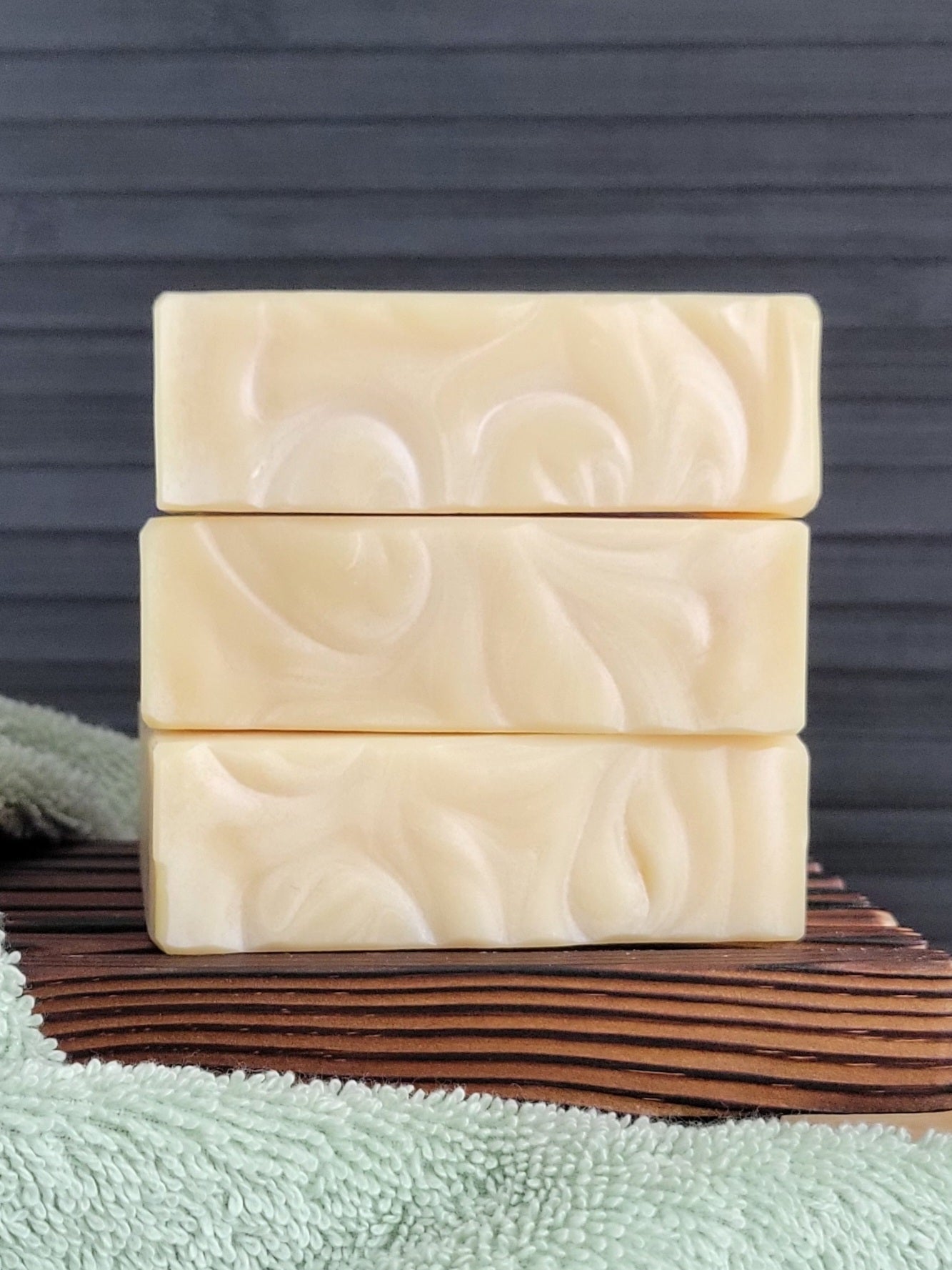 Three bars of soap with a floral pattern on a wooden block against a dark background