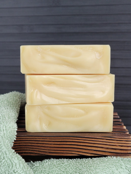 Three bars of soap stacked on a wooden block with a green towel underneath, against a dark wooden background.
