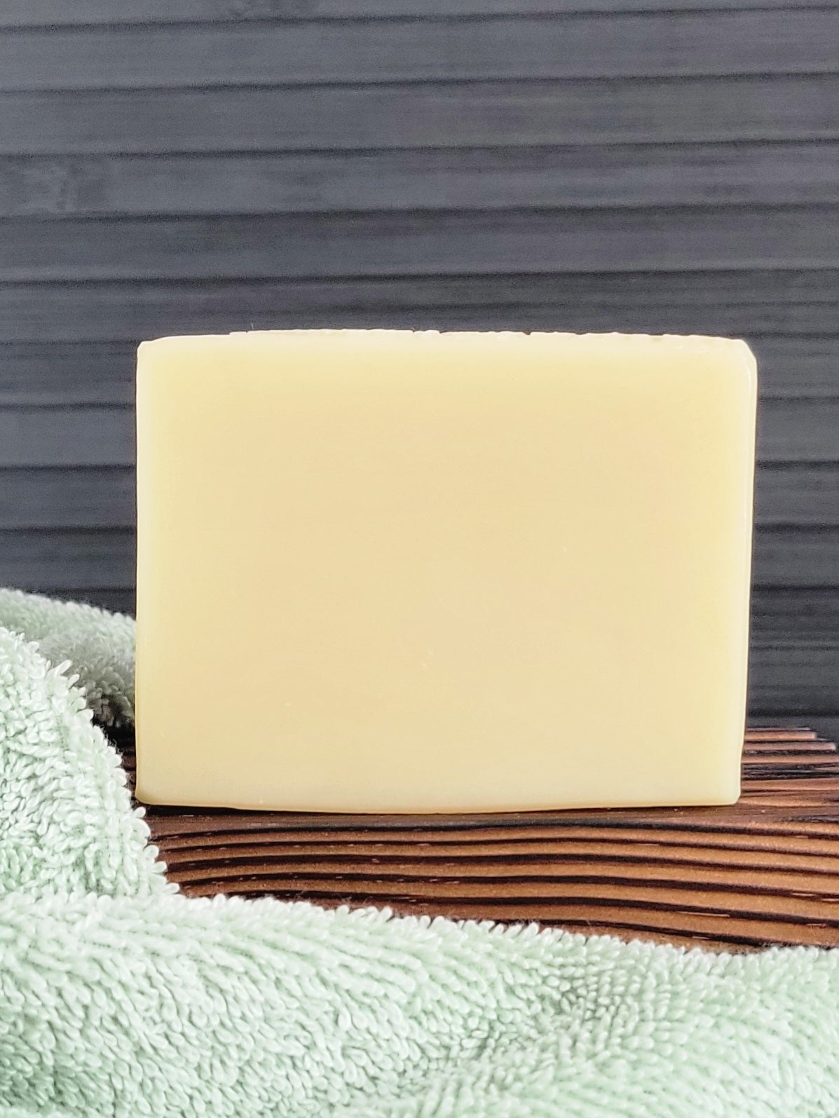 Bar of soap on a wooden soap dish with a towel underneath against a gray wall.