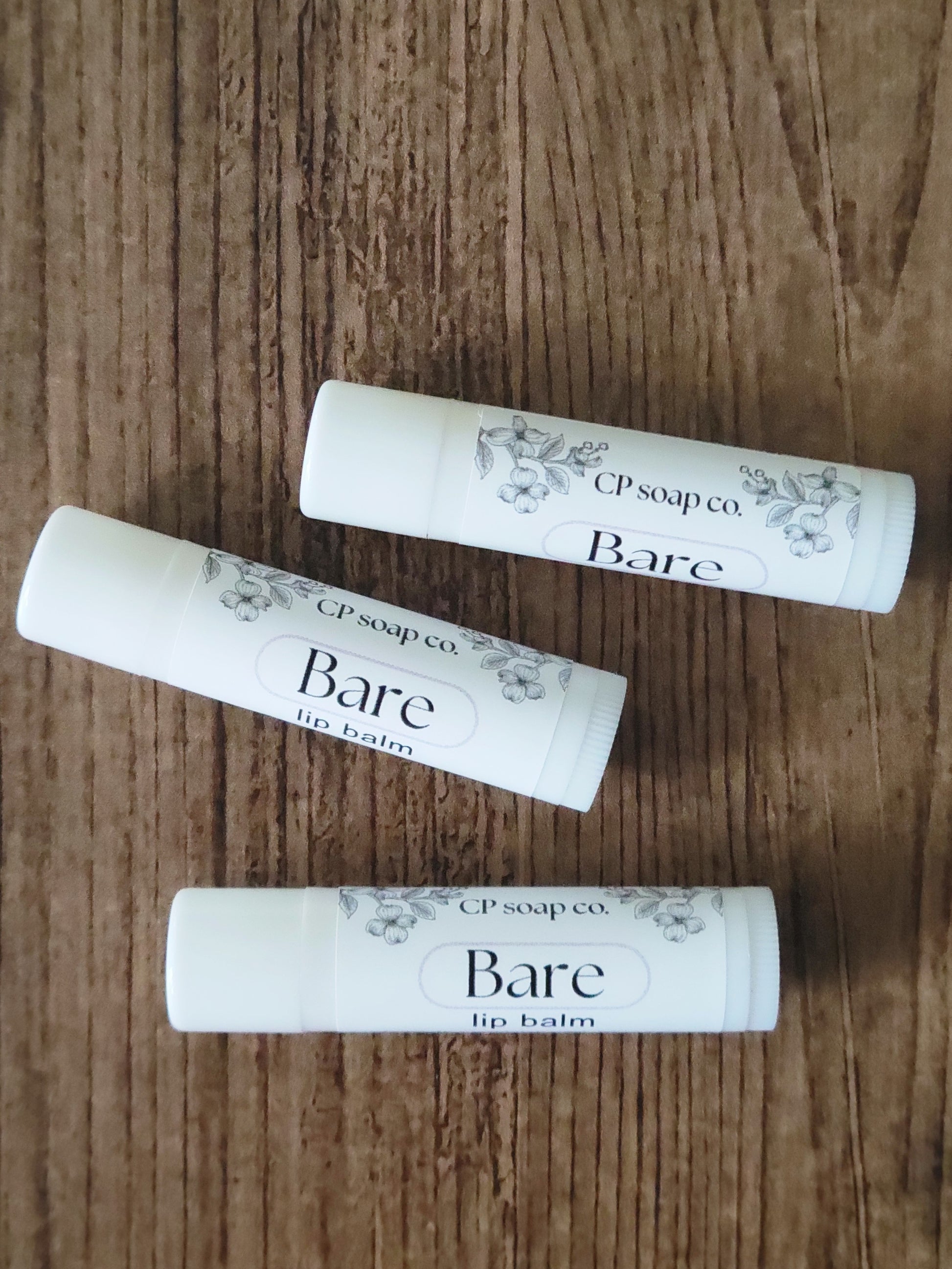 Three lip balm tubes labeled 'Bare' from CP Soap Co on a wooden surface.
