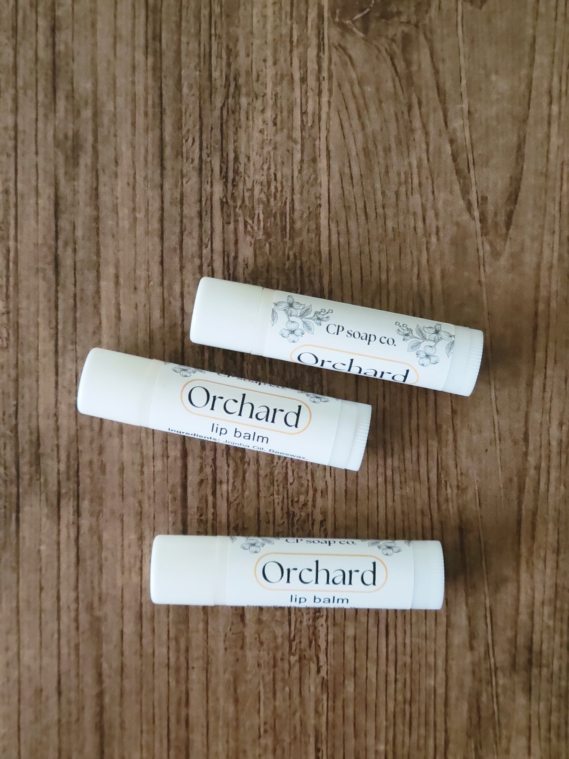 Three Orchard lip balm tubes on a wooden surface