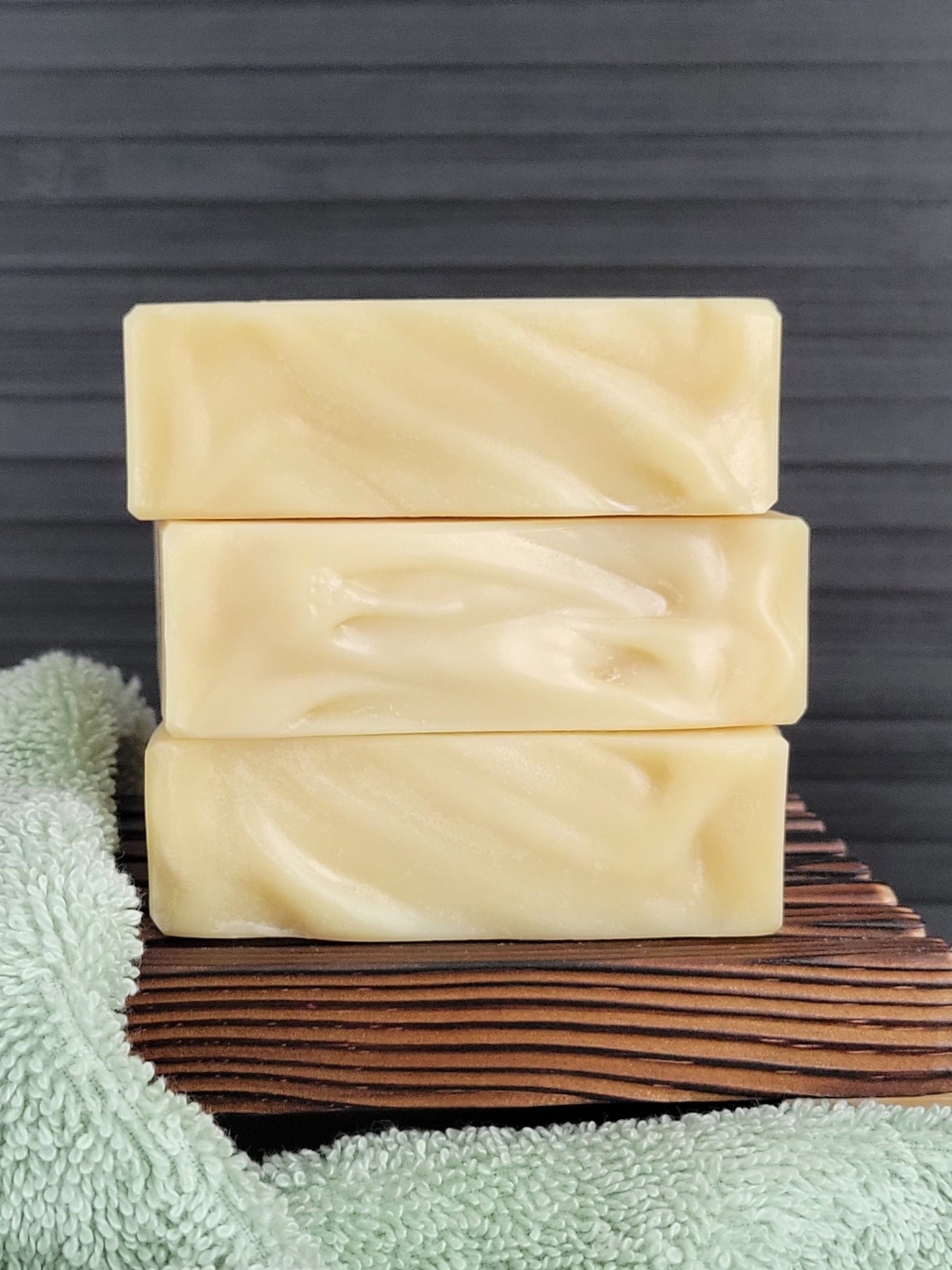 Three bars of soap stacked on a wooden block with a green towel in the background