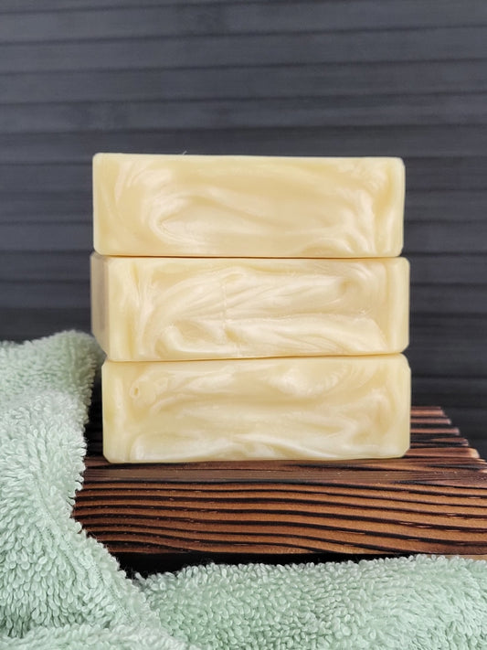 Three bars of soap stacked on a wooden block with a green towel underneath, against a dark background.